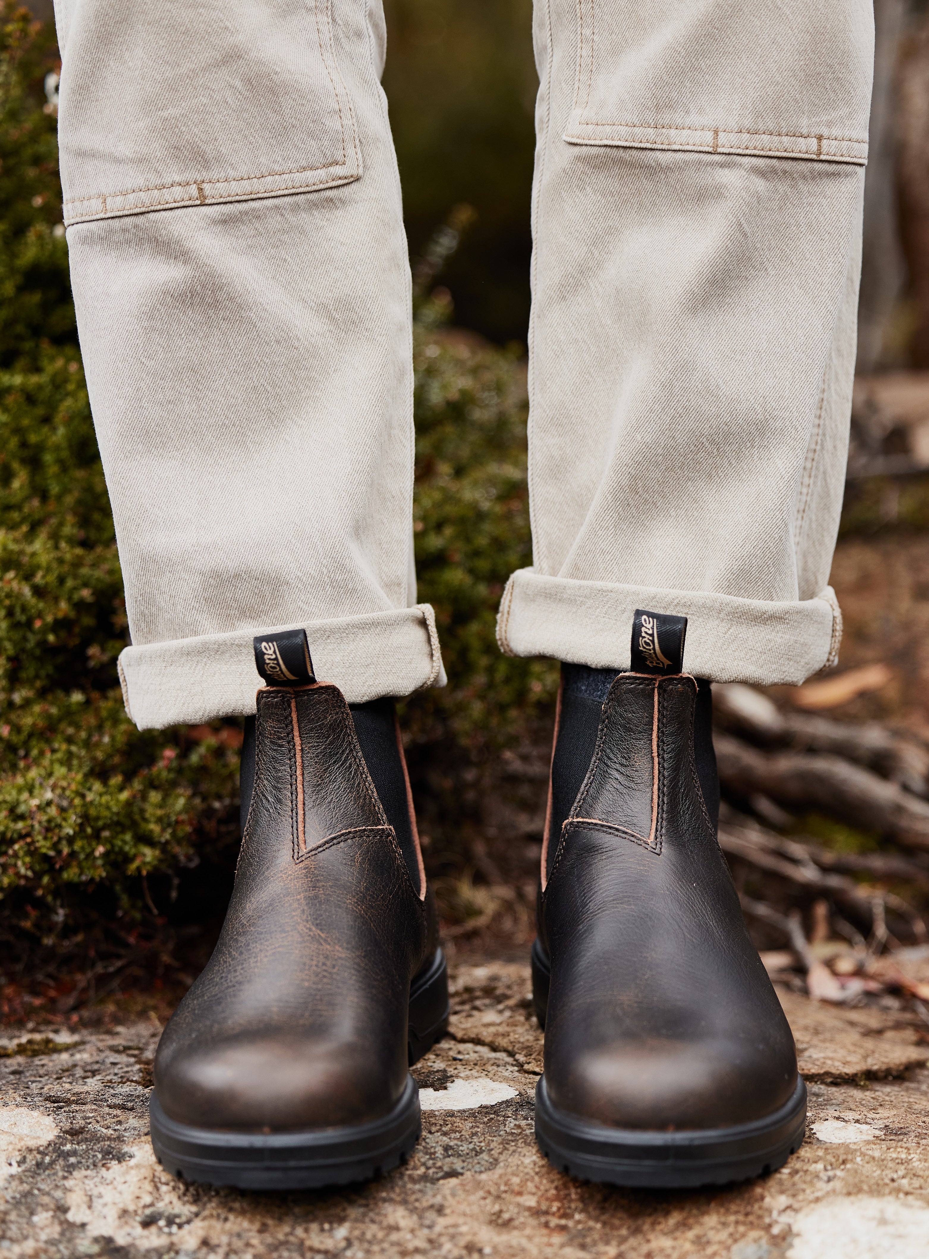 Dark brown leather boots worn with light-colored pants on a natural background